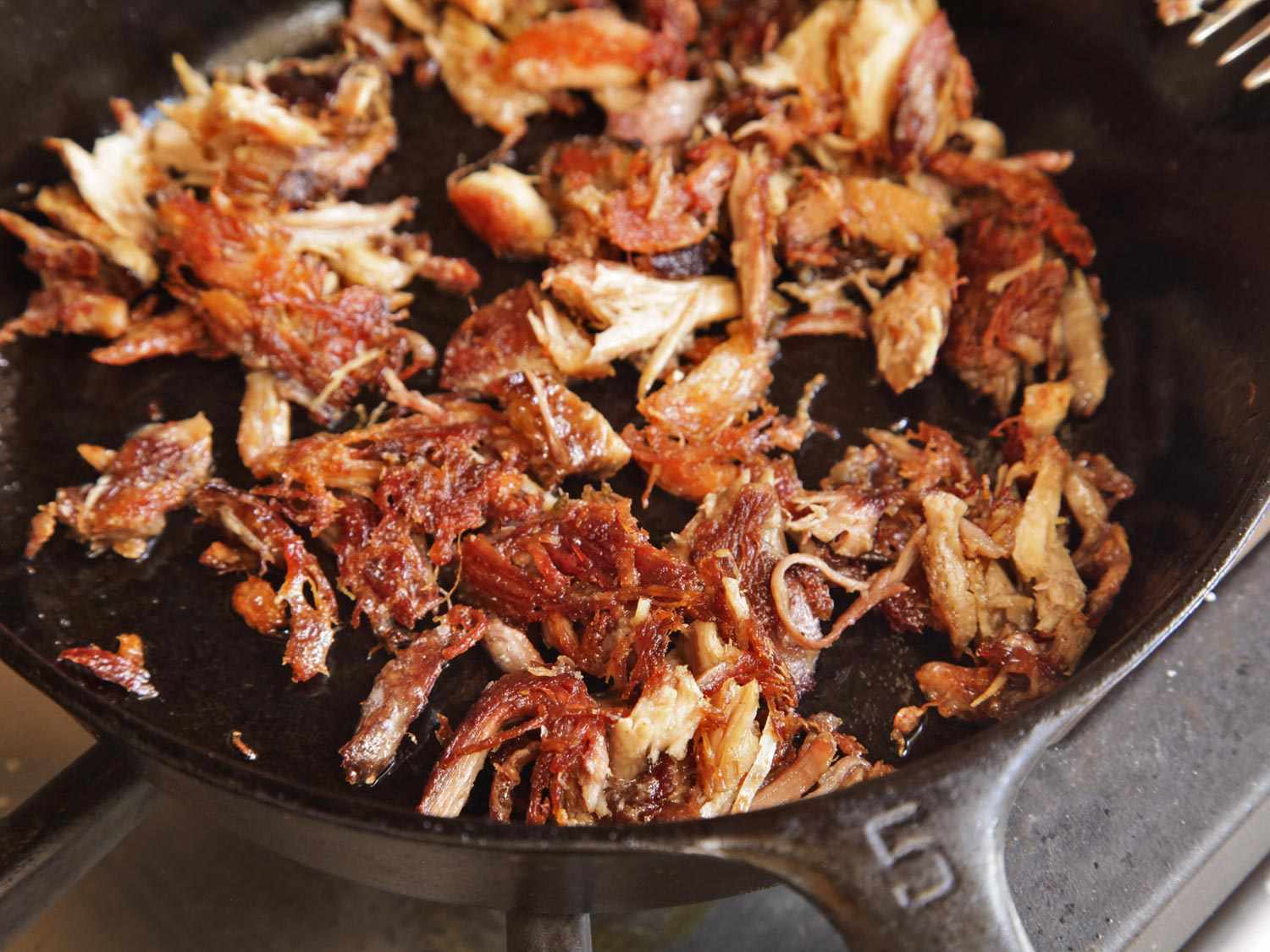 Frying shredded turkey in a cast iron skillet on a stovetop until golden brown and crisp.