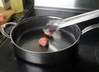 using tongs to add a meatball to a saute pan
