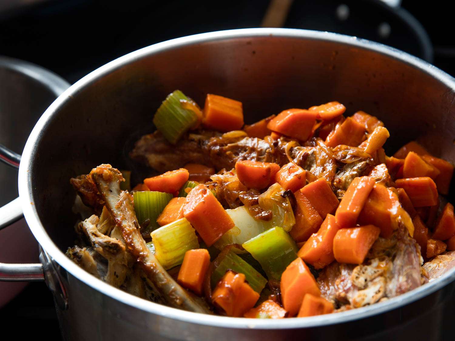 Stock pot full of roasted bones, browned vegetables, and herbs
