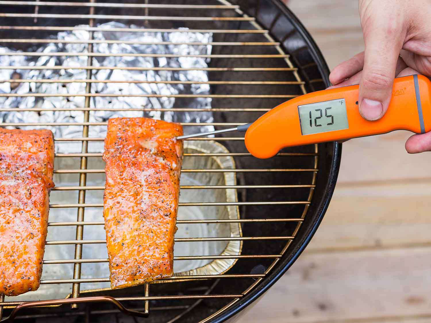 Overhead view of smoked salmon fillet portions on a charcoal grill. An instant-read thermometer inserted in the thickest portion of one fillet registers 125 degrees Fahrenheit.