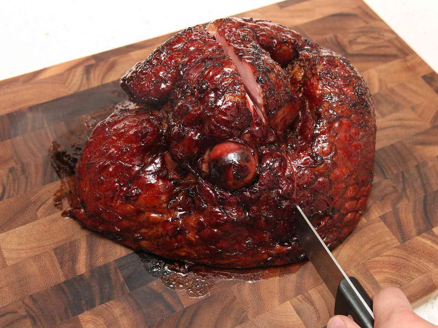 A carving knife slicing into a glazed ham on a cutting board. 
