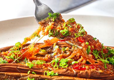 A fork lifting a piece of Chinesestyle BBQ eggplant garnished with chopped green onions on a plate