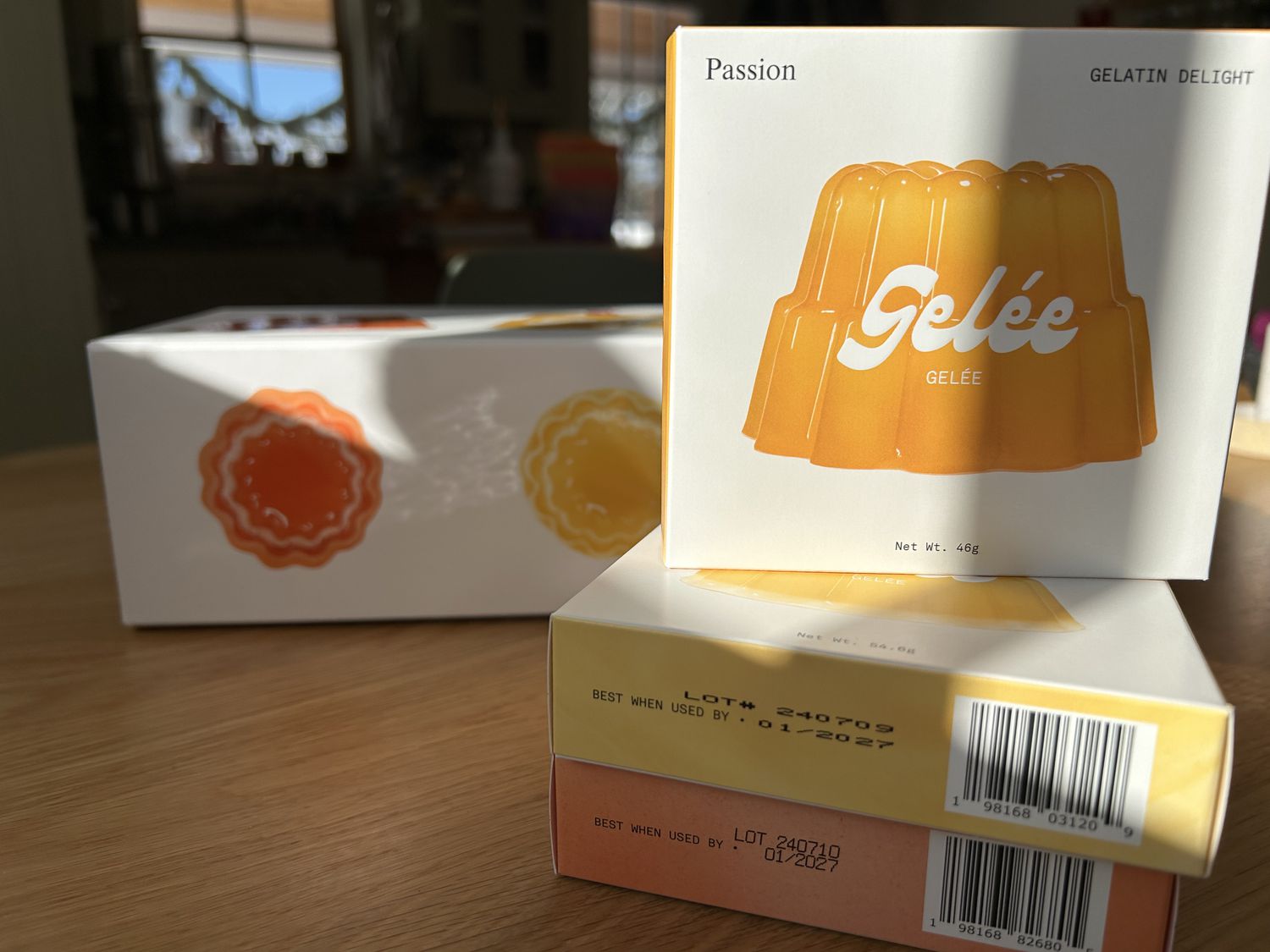 Three boxes of gelatin on a kitchen table, with a passionfruit flavored box on the top