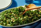A dish of roasted kale salad with wooden serving spoons on a blue tablecloth
