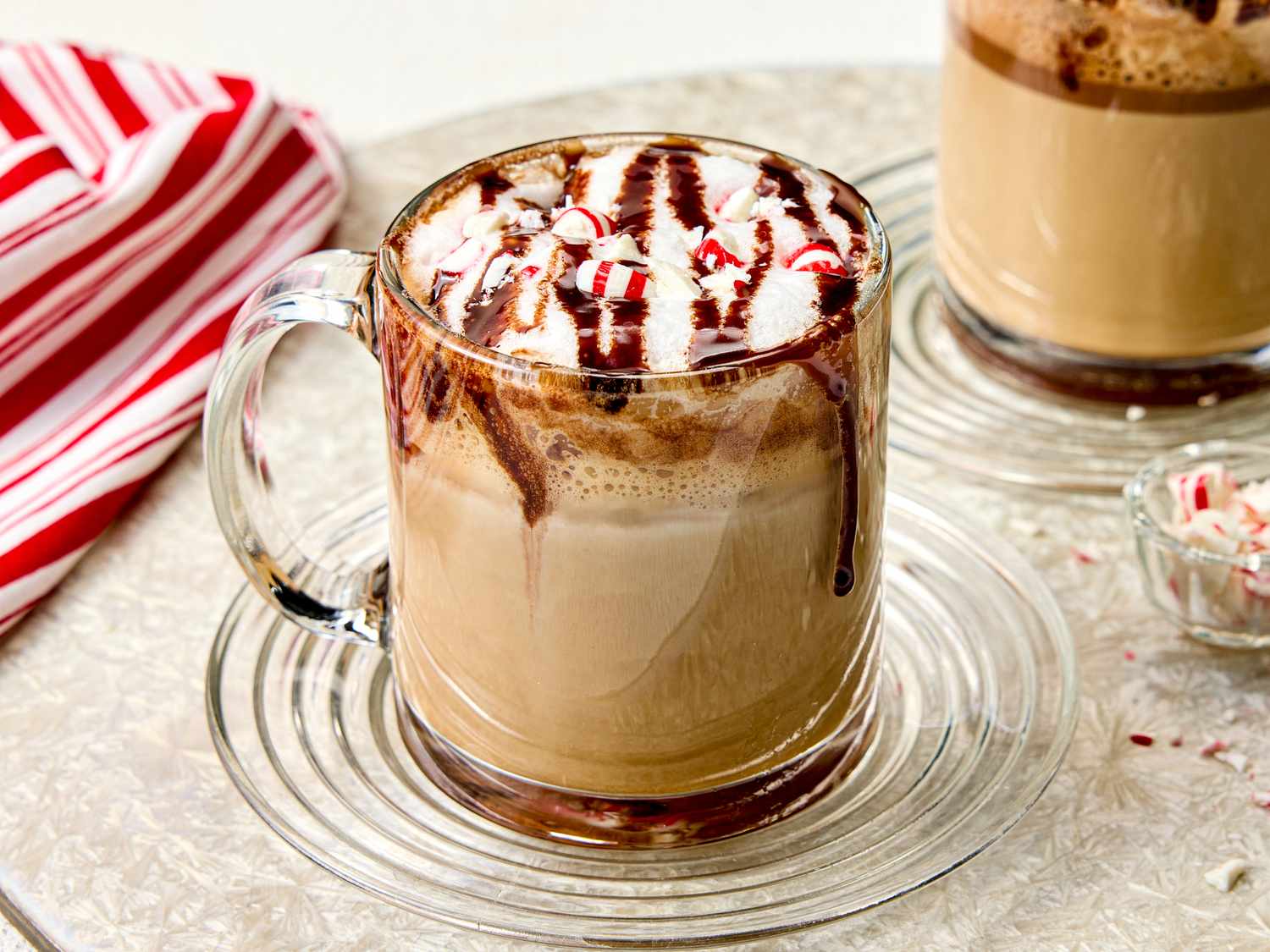 A mug of coffee topped with whipped cream chocolate drizzle and crushed peppermint candy