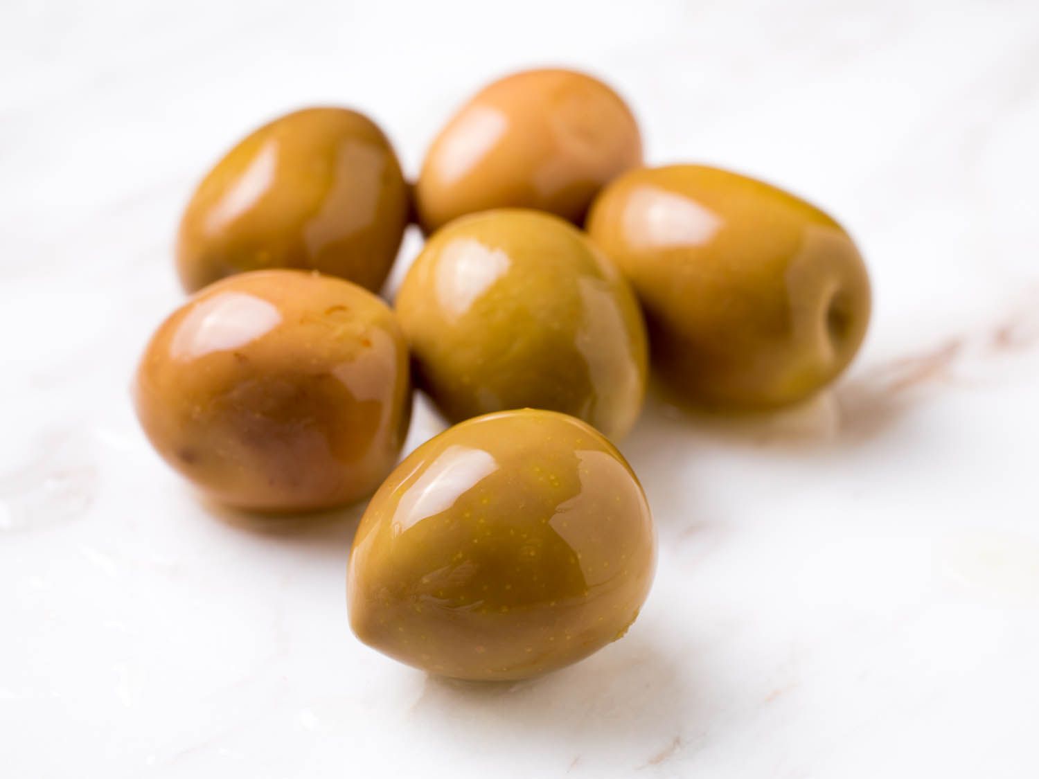 Closeup of shiny, brownish-green olives on marble surface