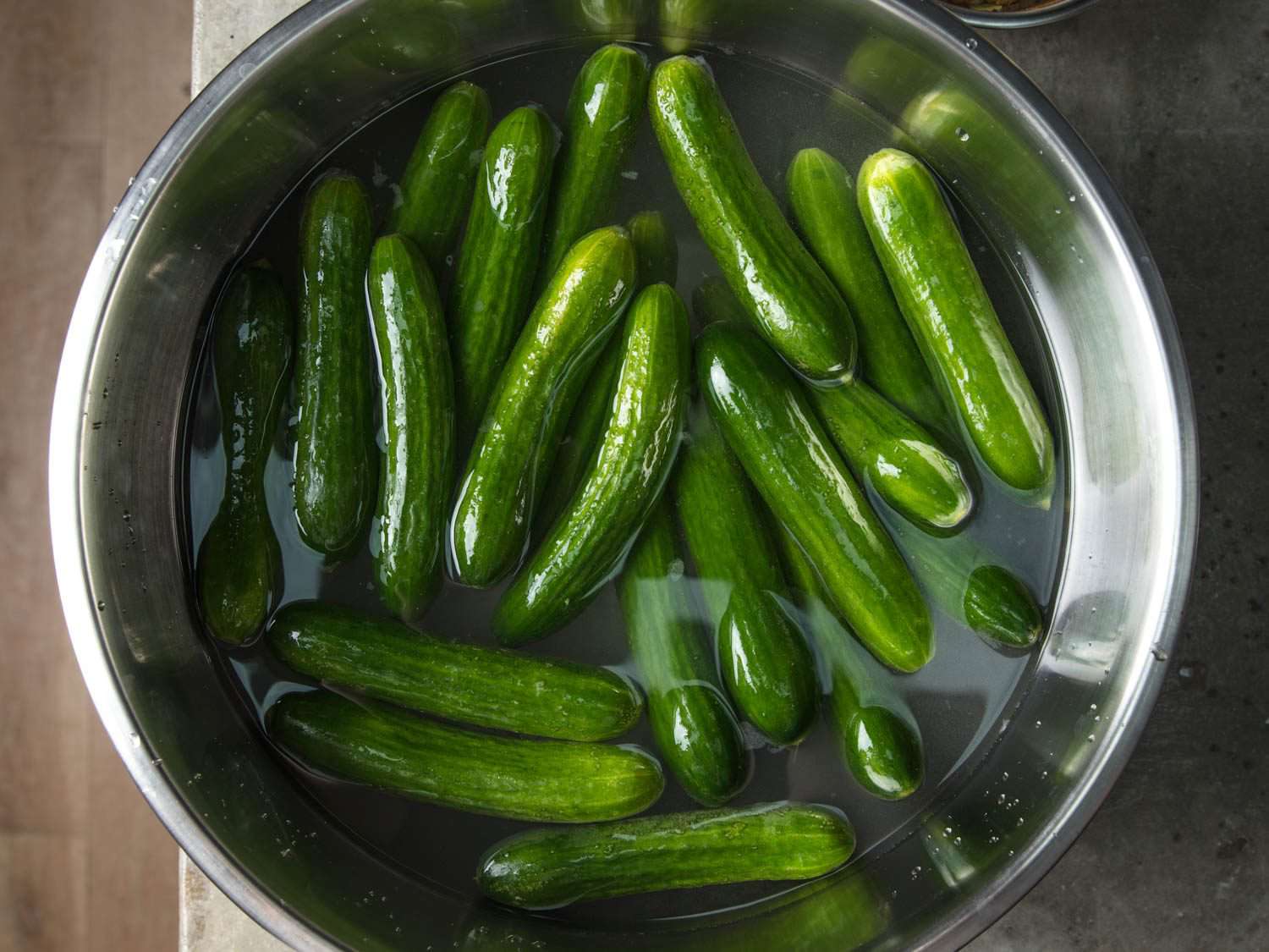 Overhead view of bowl with small cucumbers soaking in salt water as a preparatory step before pickling
