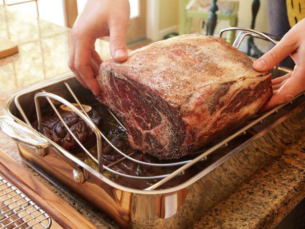 Two hands placing an uncooked prime rib roast in roasting pan.