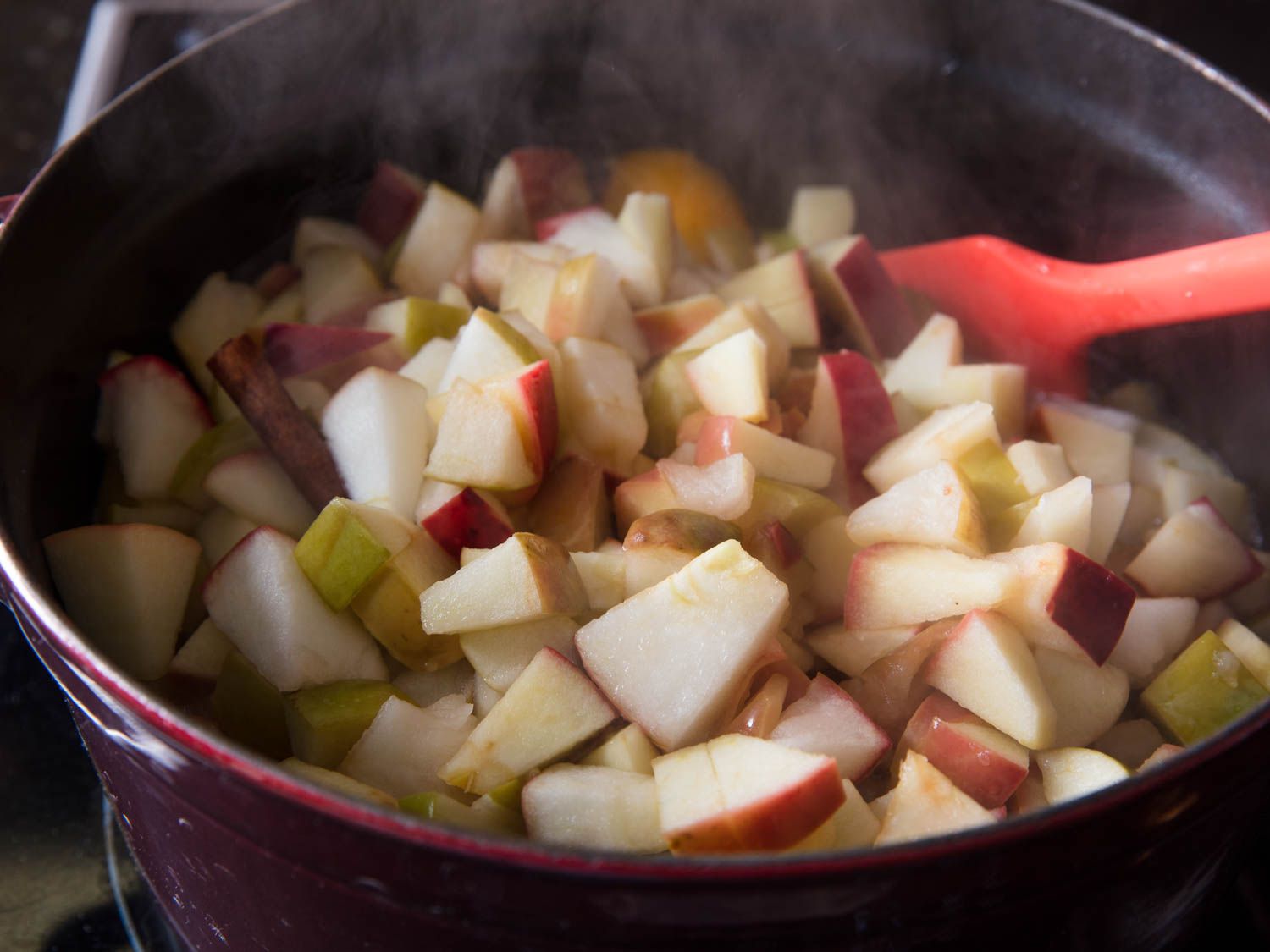 Stirring a pot of chunks of apple cooking that are down for applesauce, with a red spatula.