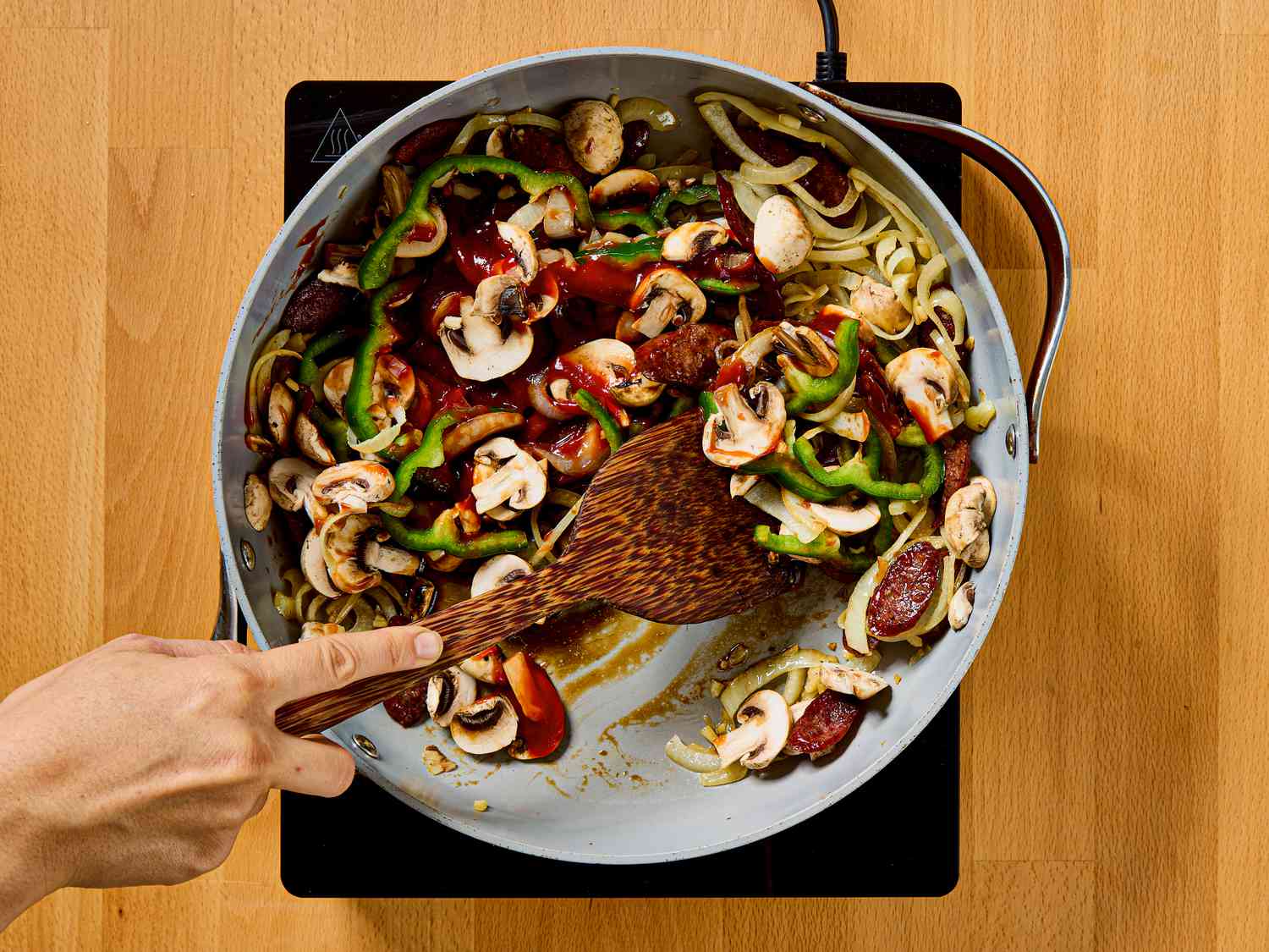 A pan of spaghetti Napolitan ingredients being cooked, showing vegetables and sausage