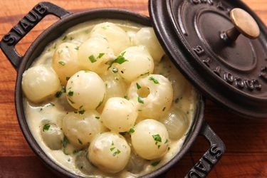 Overhead view of creamed pearl onions in a cast iron cocotte, fresh from the oven.