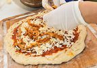 Pizza dough topped with barbecue pizza sauce and cheese is topped with pulled pork before grilling.