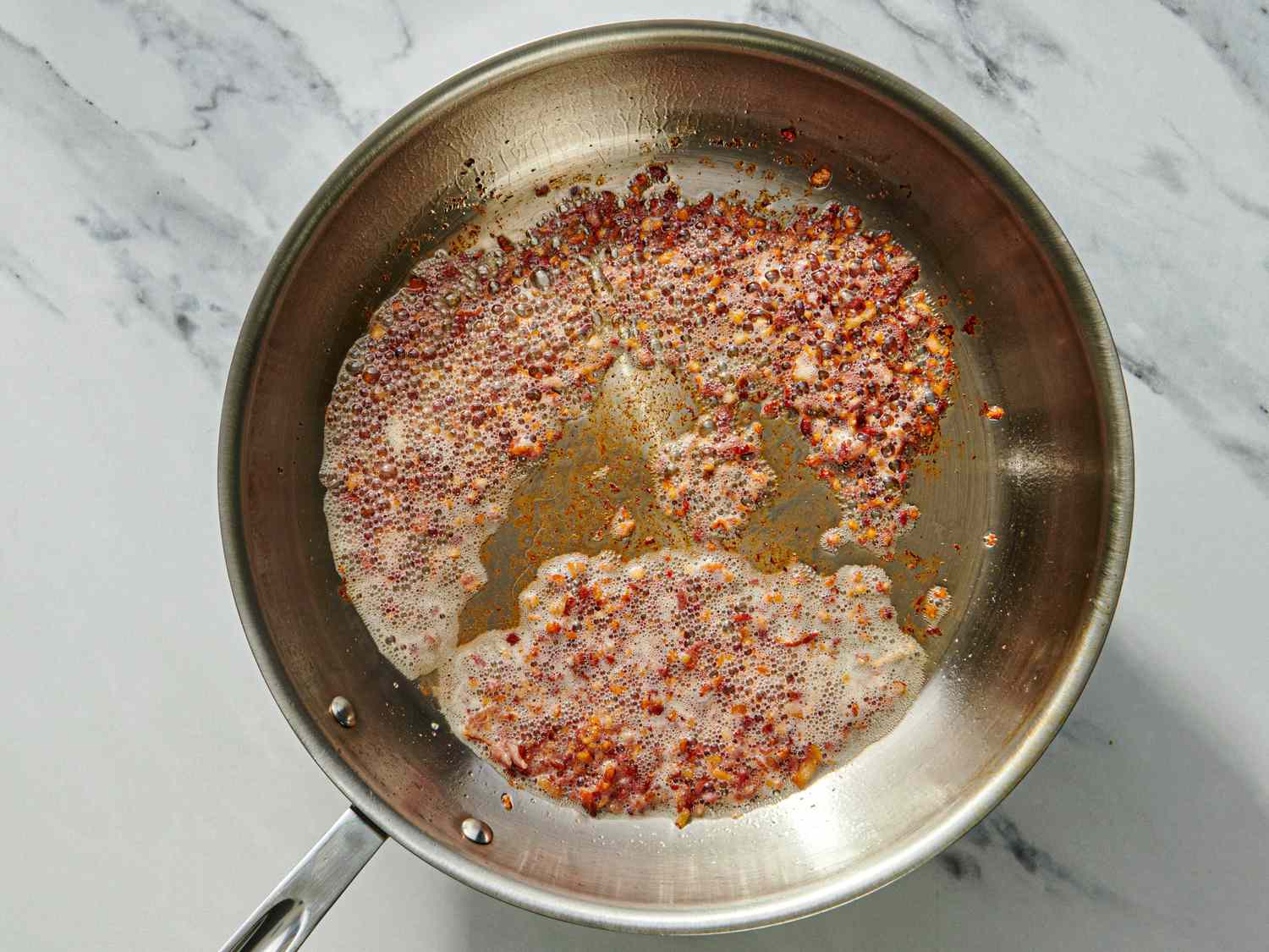 A frying pan with a bubbling mixture of seasonings including crushed red pepper