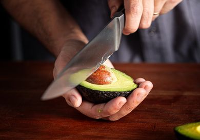 A person removing the pit from half of an avocado with a knife closeup on hands and the avocado