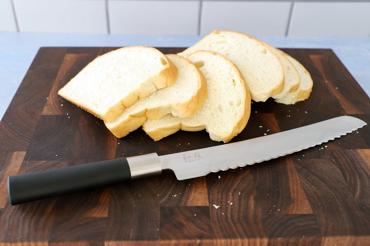 Kai Wasabi 9" Bread Knife displayed on a wood cutting board with sliced bread