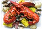 Overhead view of a lobster boil arranged on a square white porcelain platter.