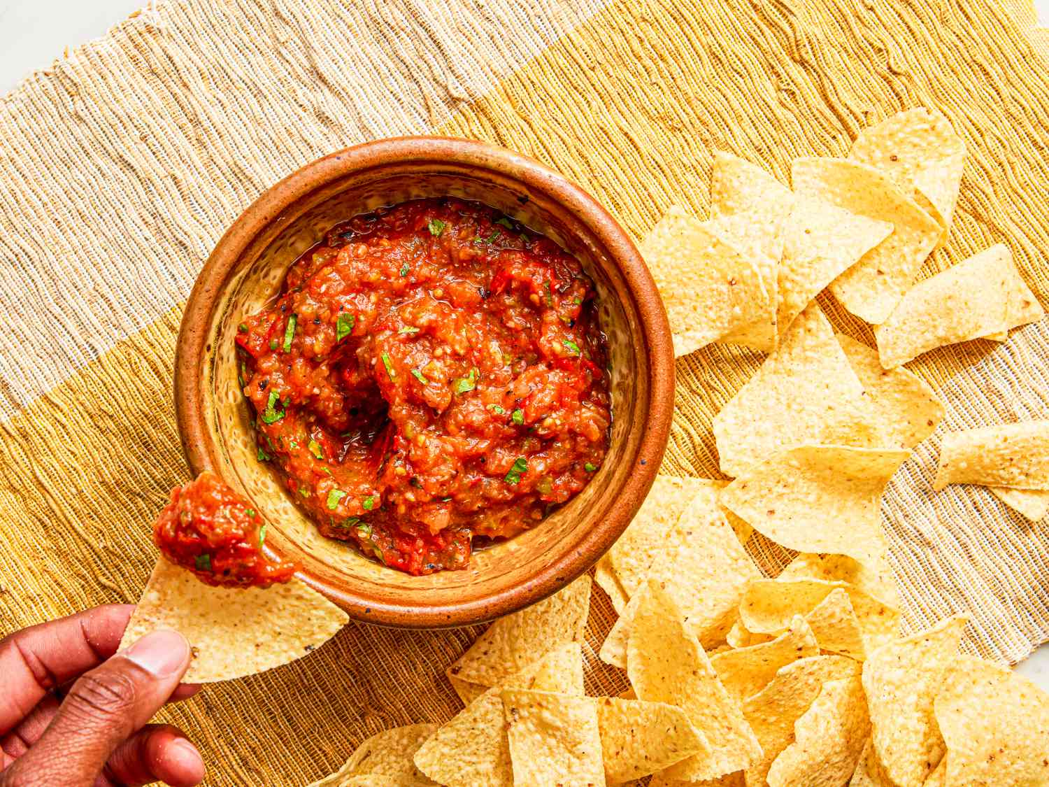 Overhead view of a hand dipping a chip in salsa 