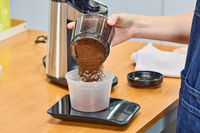 A person pours ground coffee from the OXO Brew Conical Burr Coffee Grinder With Integrated Scale into a plastic container