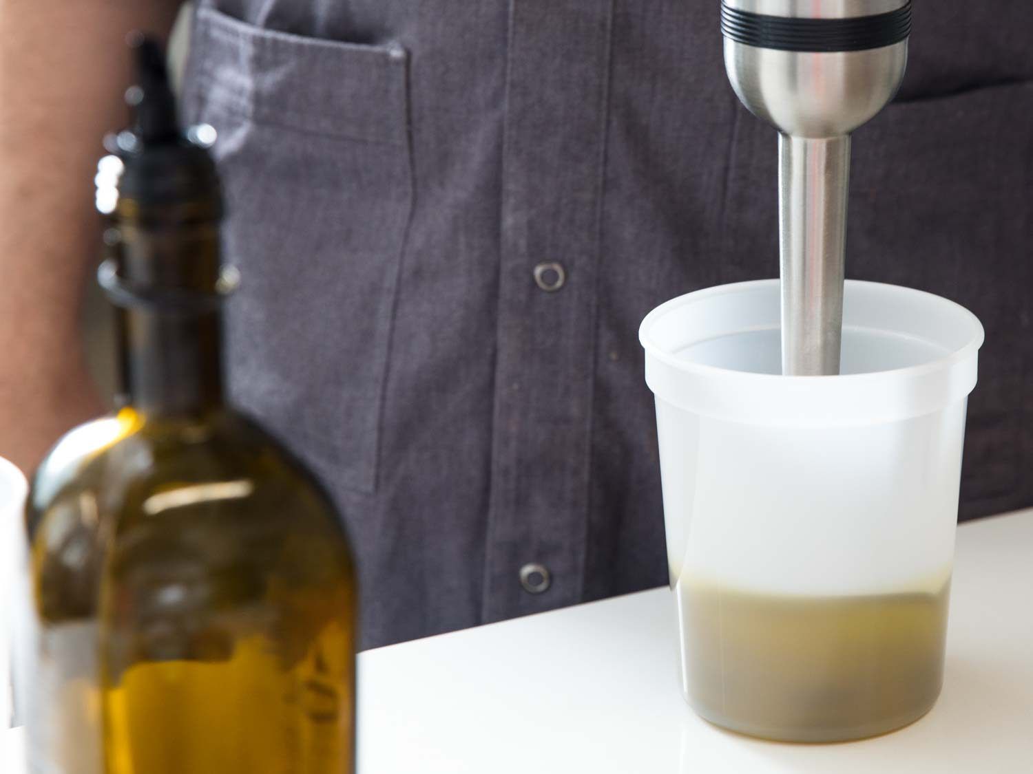 Using an immersion blender to blend an olive oil emulsion in a clear plastic container