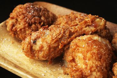 Three pieces of fried chicken on a wood rectangular plate, sprinkled with salt. 