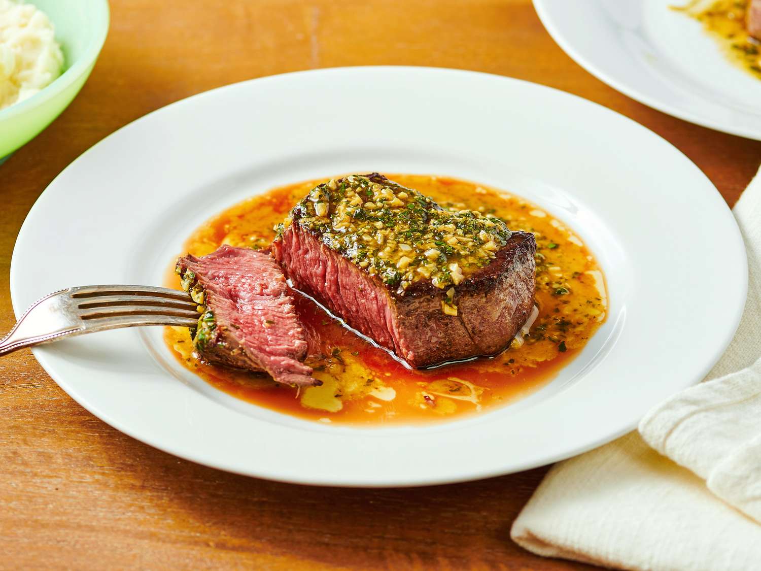 Steak topped with a garlic herb mixture on a plate, fork cutting a piece