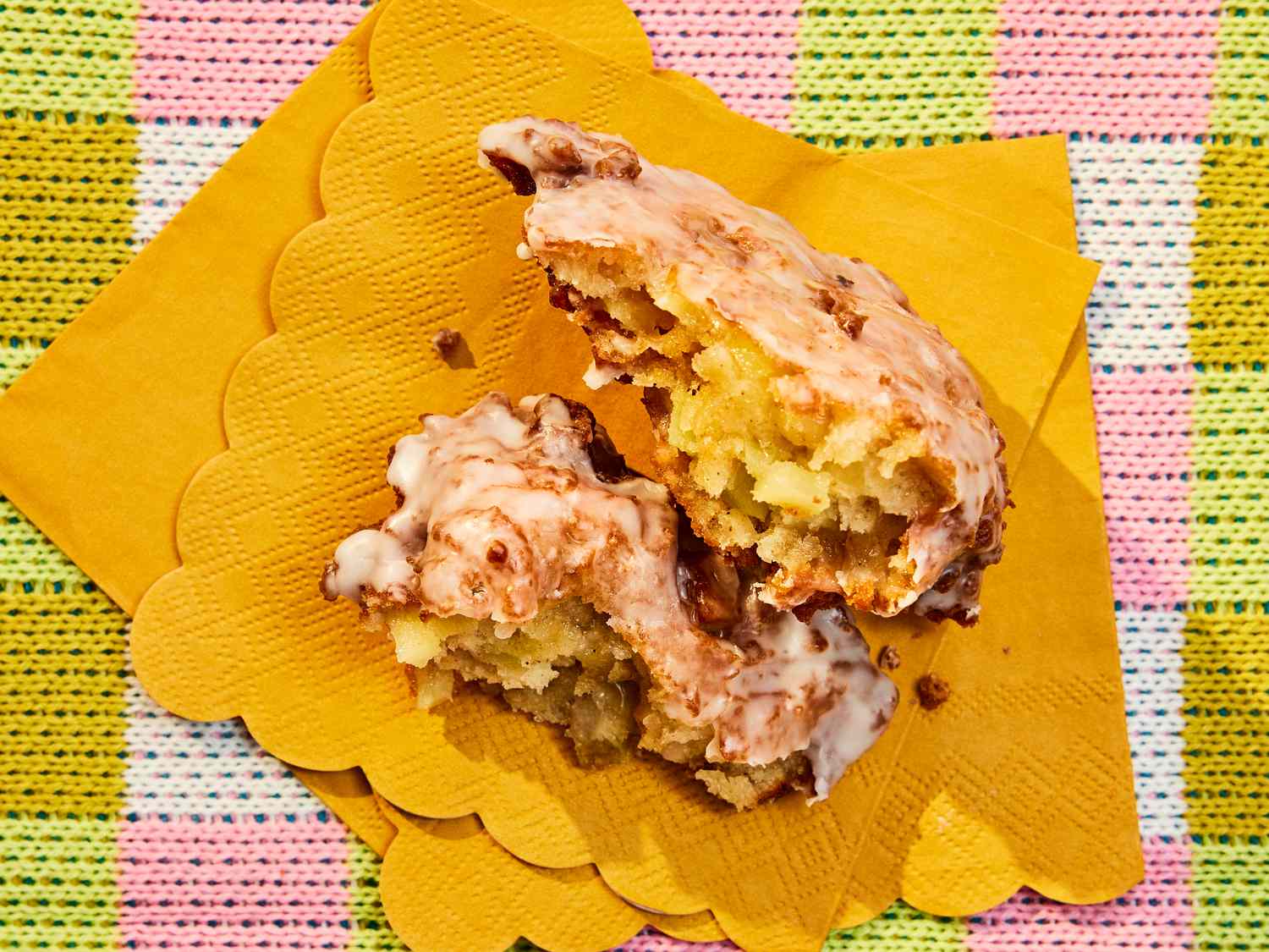 Ripped open apple fritter on yellow napkins, and a colorful checkered fabric tablecloth