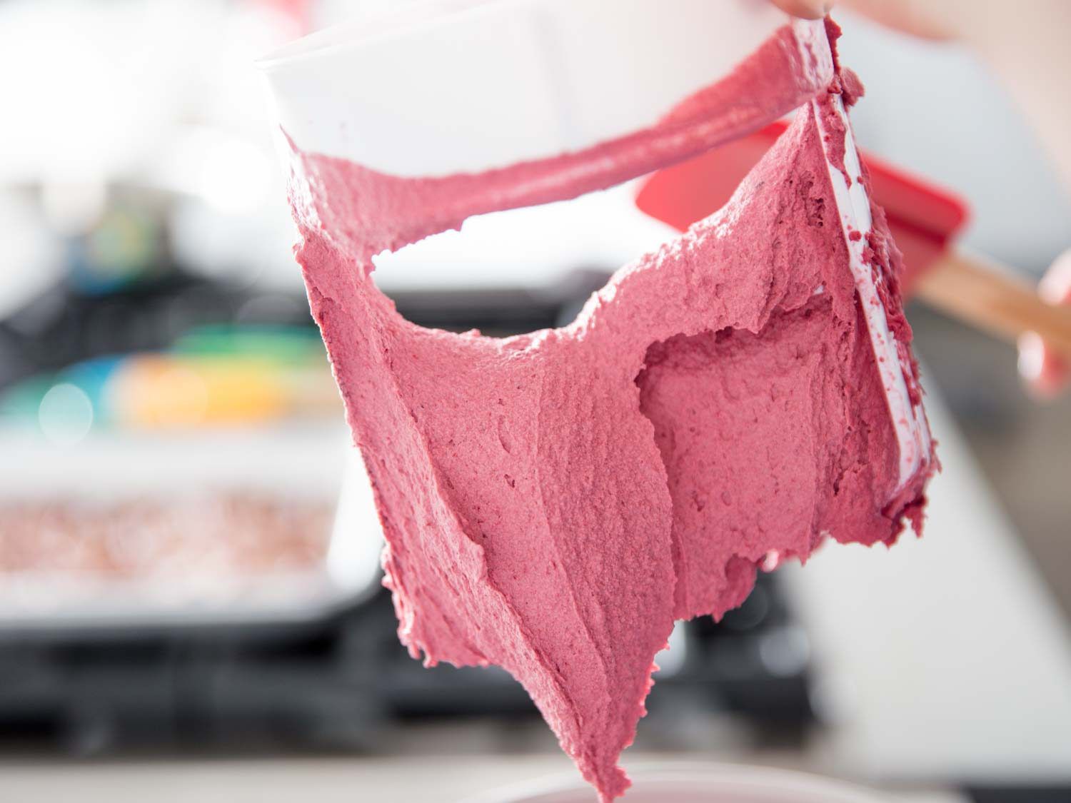 Paddle of an ice cream machine being lifted for the camera. The blackberry ice cream has finished churning and taken on a light burgundy color.