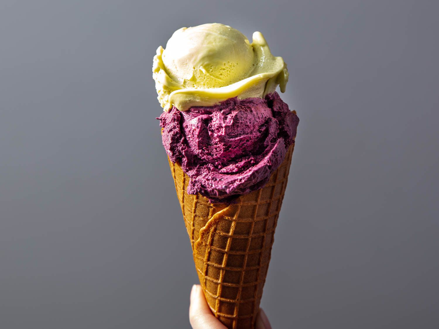 Two scoops of ice cream, one purple, one green, in a homemade waffle cone