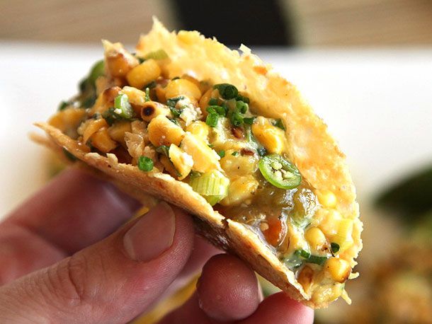 Close up of a hand holding charred corn salad and salsa verde crispy in an all-cheese taco shell.