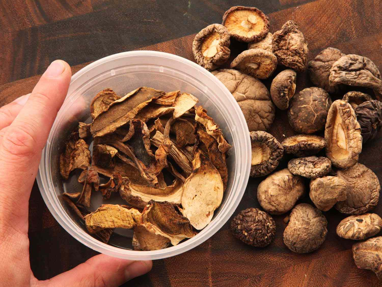 Dried porcini and shiitake mushrooms on a cutting board and deli cup.