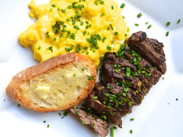 Overhead view of a plate of Herb-Marinated Steak and Soft Scrambled Eggs, served with a slice of buttered toast and showered with chopped chives.