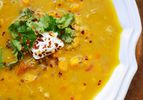 An overhead close-up of bright orange mulligatawny soup garnished with chile flake, fresh cilantro leaves, and a dab of yogurt.