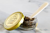 An open jar of Olma osetra caviar with a mother-of-pearl spoon inside