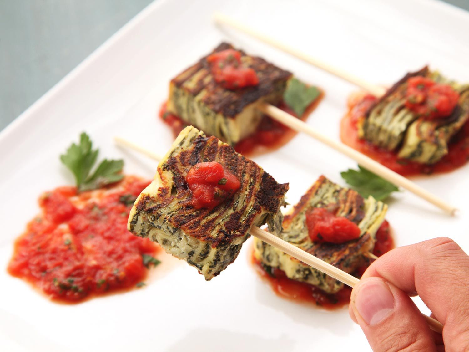 Hand picking up a skewer of crispy leftover lasagna from a platter