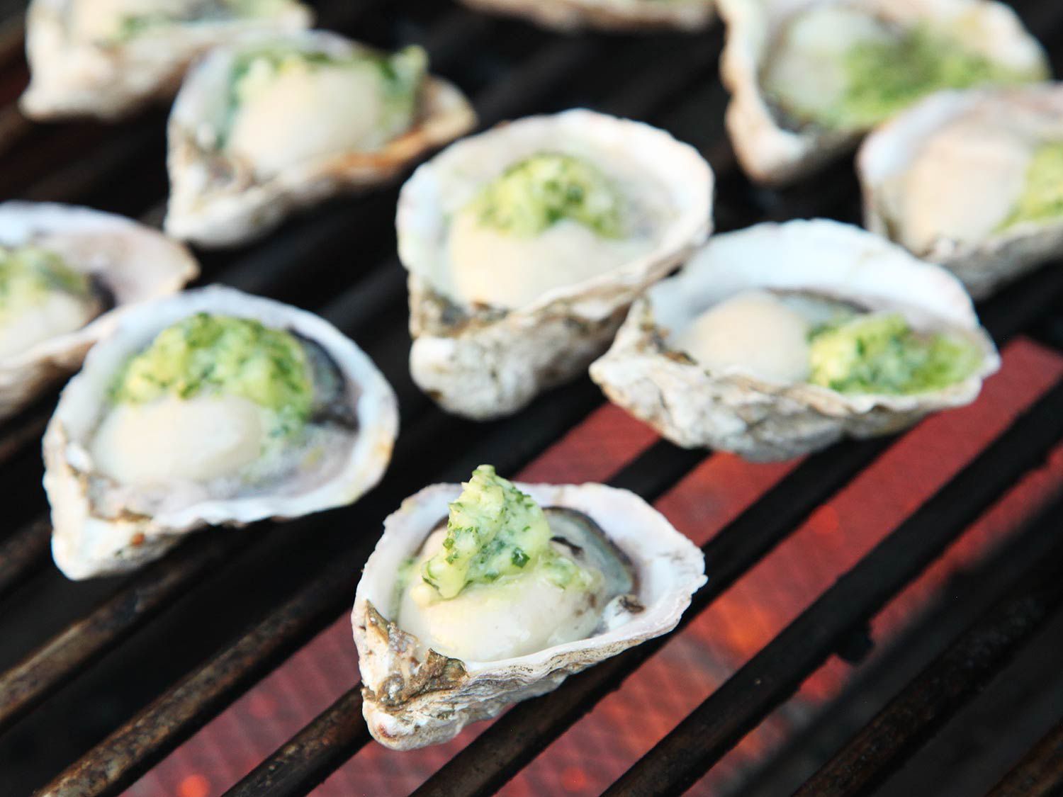 Oysters on the half shell topped with compound butter on a hot grill.