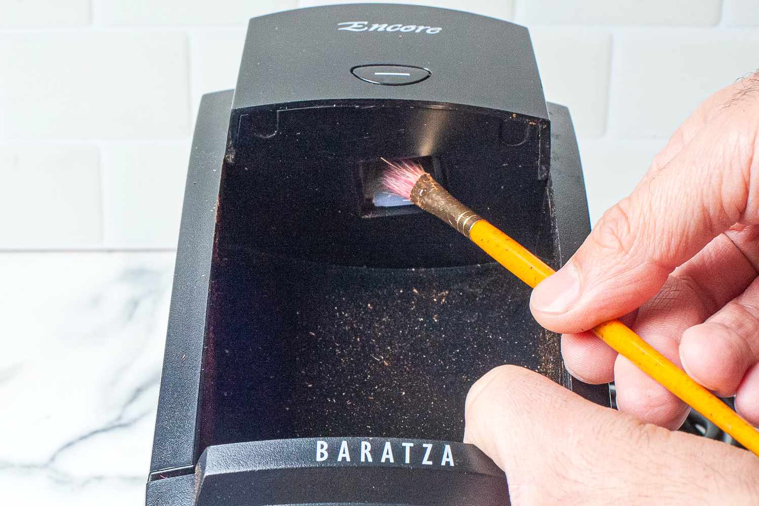 A hand using a brush to clean the inside of a Baratza coffee grinder hopper.
