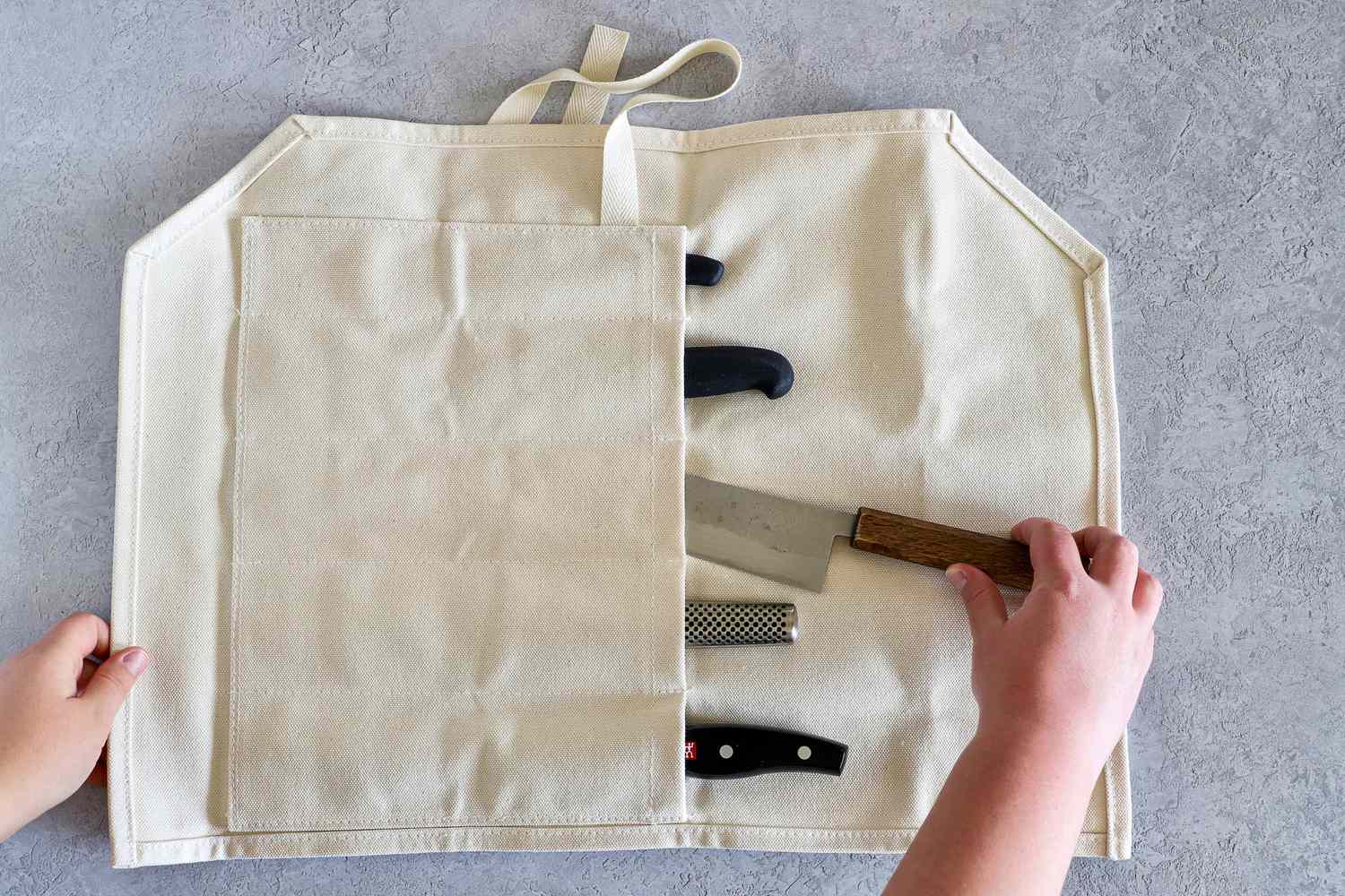 A fabric knife roll with knives inside hands organizing the knives