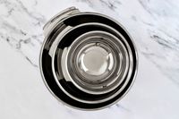 A set of stainless All-Clad mixing bowls stacked together placed on a marble surface