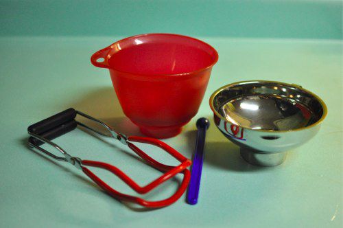 Tongs, a wide-mouth funnel, a variety of measuring cups, and jar lifter resting on a table.