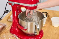 A person removes the whisk attachment on the KitchenAid 7 Quart Bowl Lift Stand Mixer