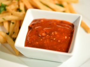 A square ramekin of orange chipotle ketchup flanked by a pile of french fries.
