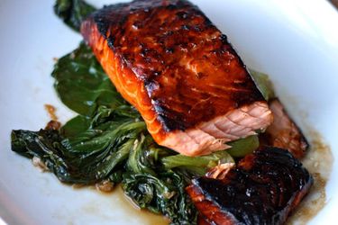 Teriyaki-glazed salmon on a bed of wilted bok choy on a white serving dish.