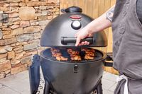 A person closes the top on the Char-Griller E16620 Akorn Kamado Charcoal Grill