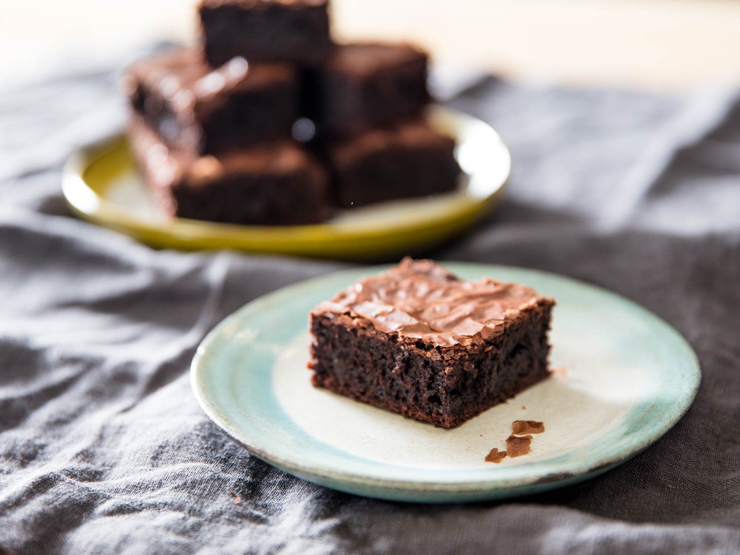 A single brownie on a plate, with a plate of more brownies in the background