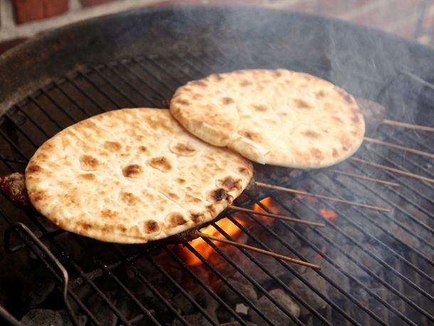 Two pieces of flatbread heating up on top of kebab on a grill. 