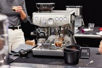 The Breville Barista Express Impress brewing an espresso and a person holding an espresso in their hand