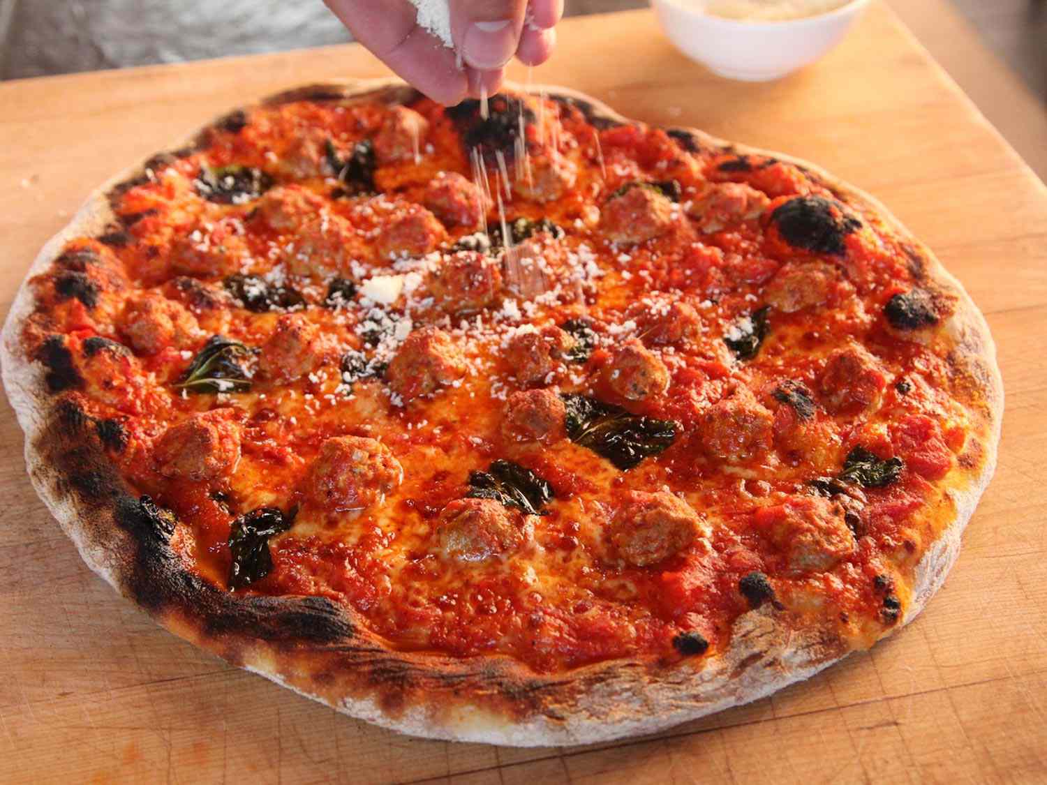 Sprinkling grated Pecorino Romano on a cooked meatball pizza.