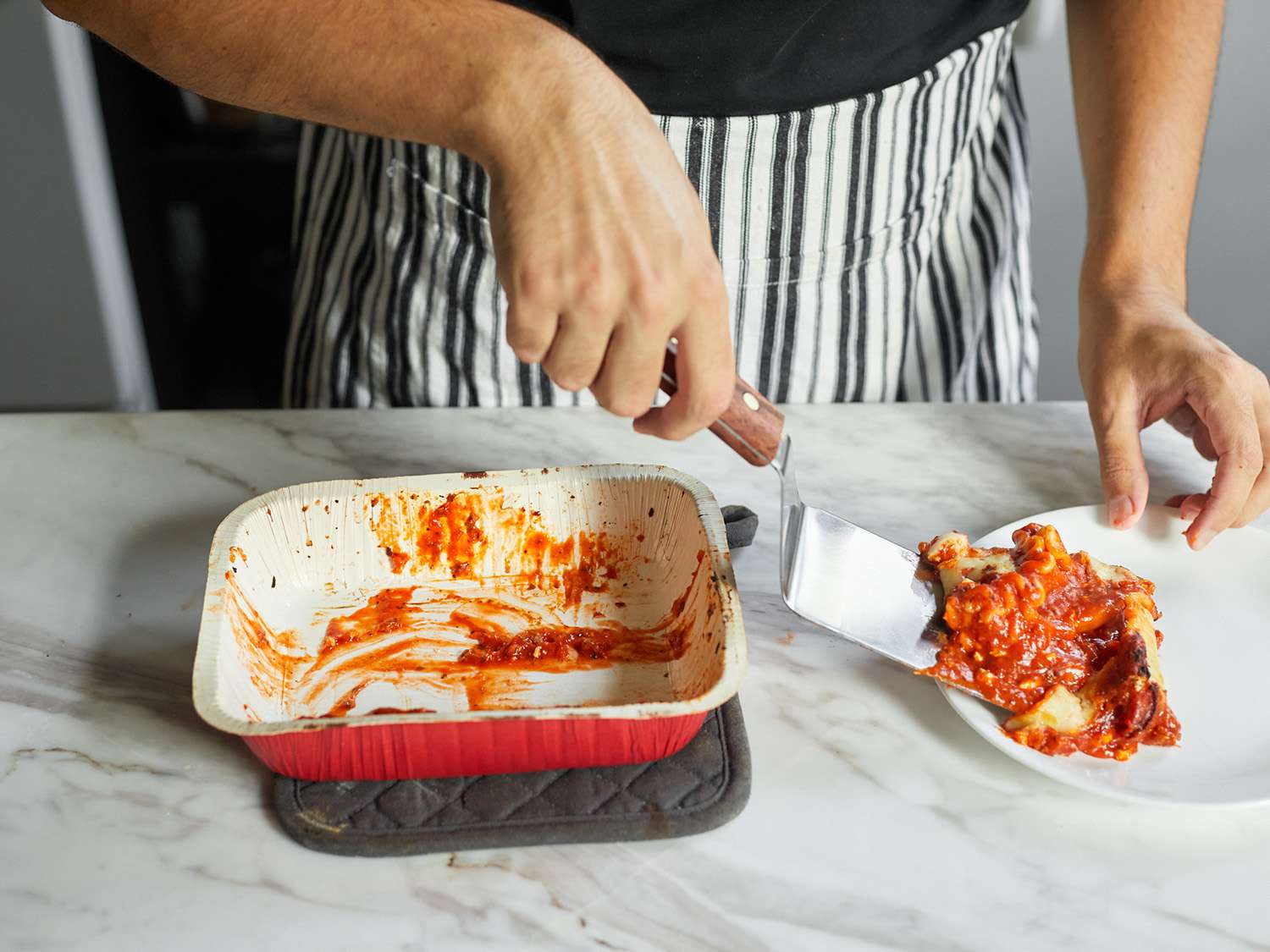 A person using an offset metal turner to serve a piece of lasagna
