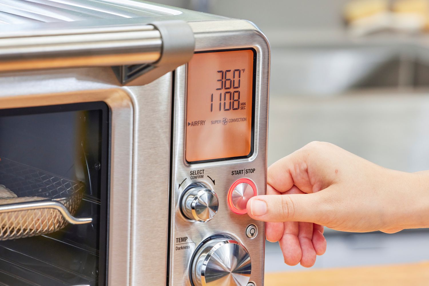 A thumb touching a button on the Breville the Smart Oven Air Fryer