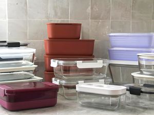 A collection of various food storage containers in different shapes and sizes stacked on a kitchen counter against a tiled backsplash